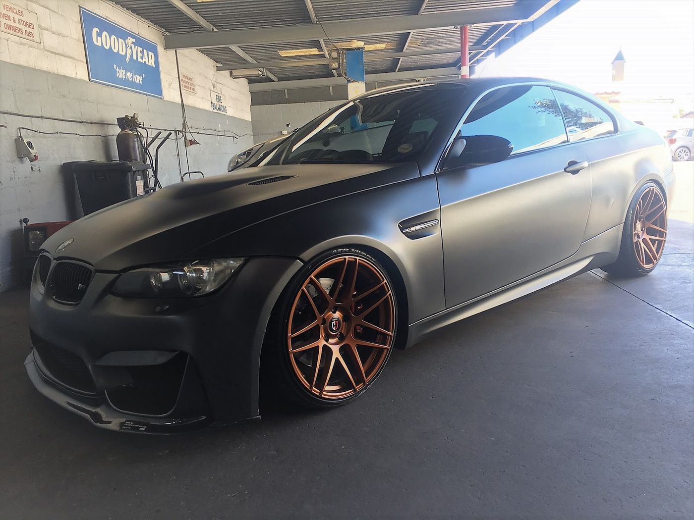 Matte black BMW M3 with bronze wheels in the workshop